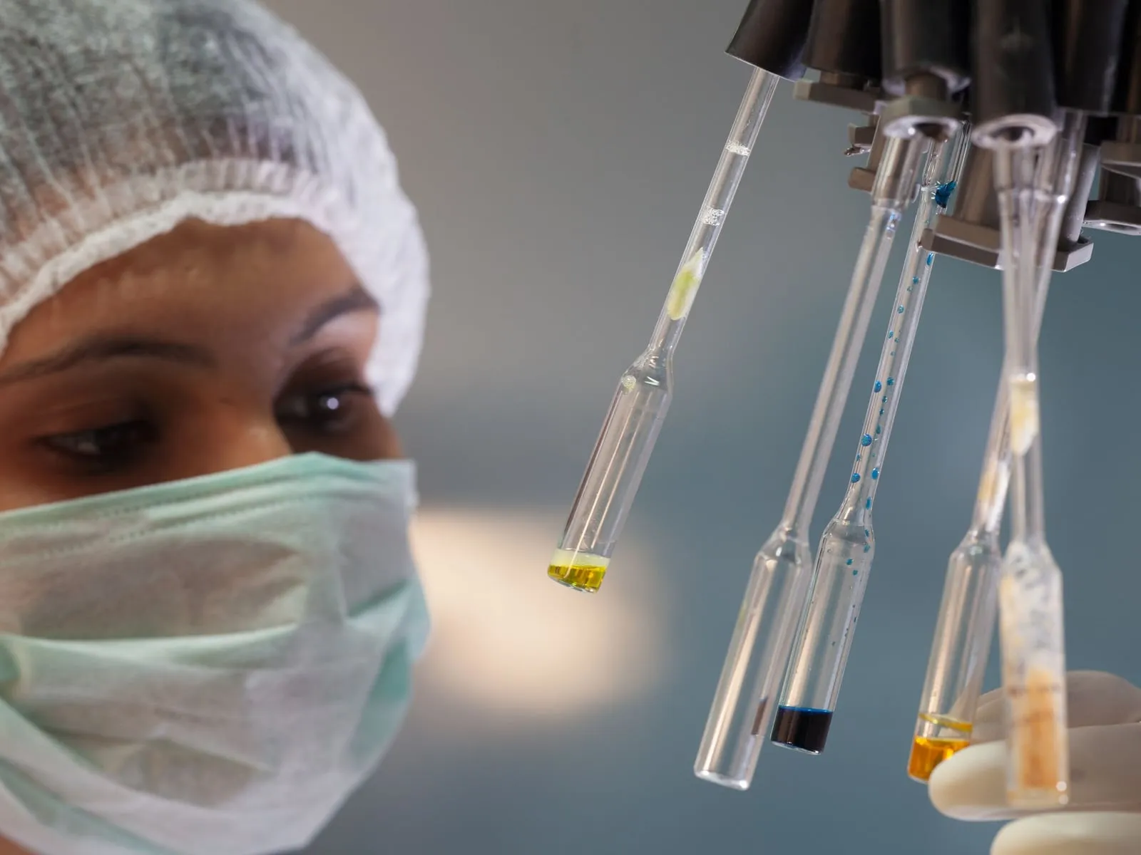 Laboratuvarda maske ve bone takan araştırmacı test tüplerini inceliyor